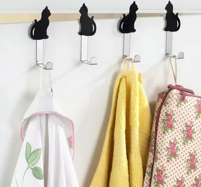 Four cat-shaped hooks on a wall with items hanging on them.