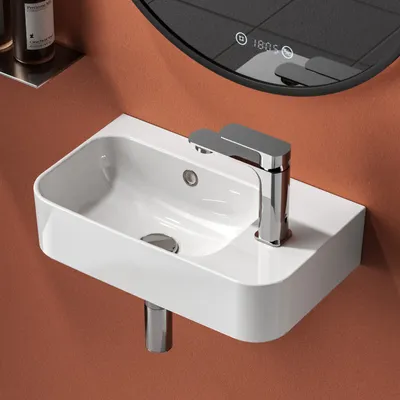 A close-up shot of a white ceramic wall-mounted sink with a chrome faucet against a terracotta-colored wall.
