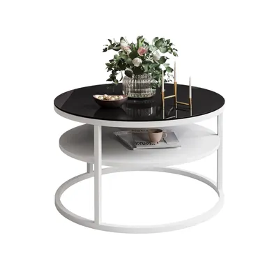 A round coffee table with a black glass top and a white shelf below, decorated with a vase of flowers and a bowl of fruit.
