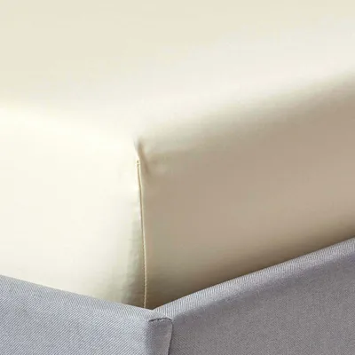 Close-up view of a fitted sheet on a bed, showing the corner and the bed skirt.