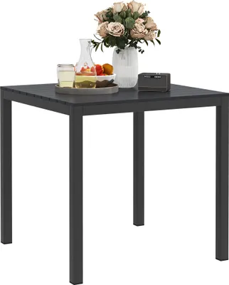 A square outdoor table with a bouquet of flowers, a glass of drink, and a small electronic device on it.