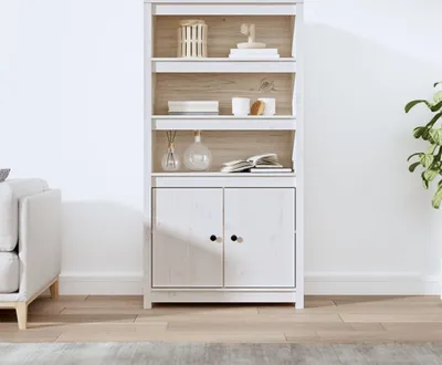 A white wooden highboard with shelves and cabinets, decorated with a few items, placed in a room with a sofa and a plant.