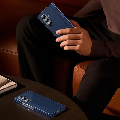 A person is holding a blue foldable smartphone while sitting on a couch. Another phone is on a table in the foreground.