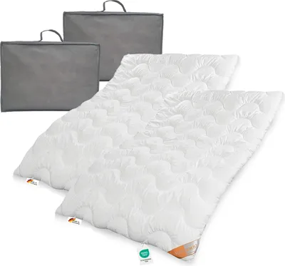Two white duvets are laid out diagonally on a white background, with two grey storage bags behind them.