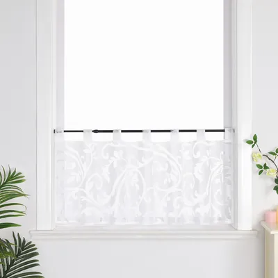 A white sheer curtain with a floral pattern hangs on a black rod in a window.