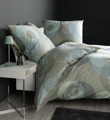 A bed with bedding and pillows, a bedside table with a lamp and a vase of flowers.