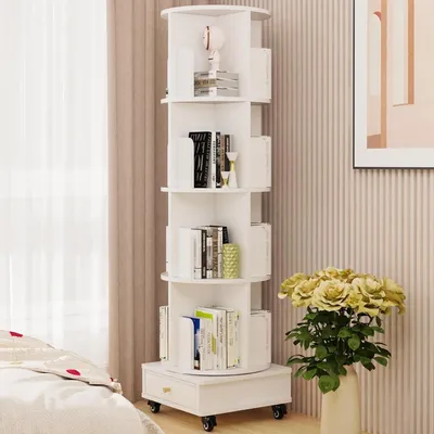 A white rotating bookshelf filled with books and decorative items, placed next to a bed and a vase of flowers.