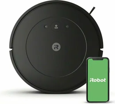 A black iRobot robotic vacuum cleaner is shown in the center of the frame, with a smartphone displaying the 'iRobot' app to its right. The vacuum has the 'i' logo on its surface and illuminated control buttons.