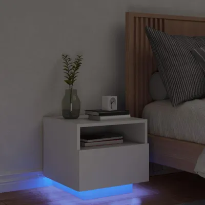 A modern white nightstand with LED lighting next to a bed.