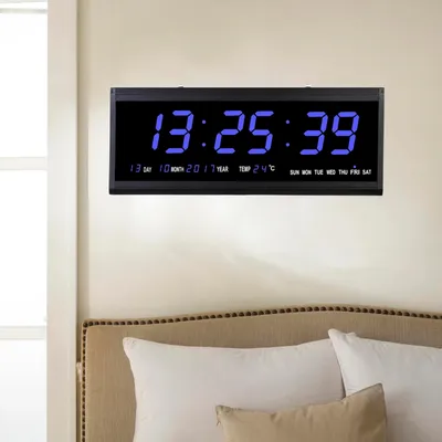 A digital clock mounted on a wall above a bed.