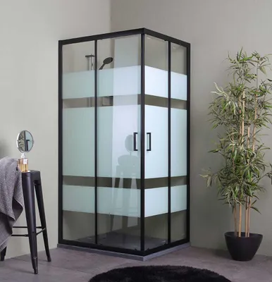 A modern bathroom corner with a shower cabin, a stool with a towel and mirror, and a potted plant.