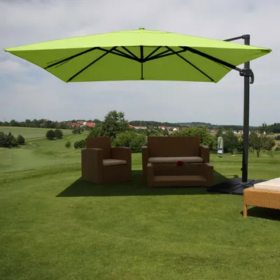An outdoor patio set with a large green umbrella, chairs, and a sofa on a grassy lawn with a scenic background.