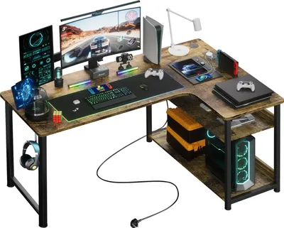 A corner gaming desk setup with multiple monitors, a computer, gaming consoles, and accessories.