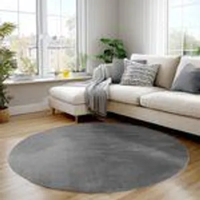 A round gray rug is placed on a wooden floor in front of a sectional sofa in a living room.
