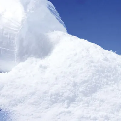 A pile of artificial snow is being poured out of a clear plastic bag against a blue sky background.