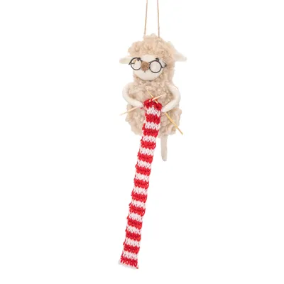 A knitted sheep ornament with glasses, knitting a red and white striped scarf.
