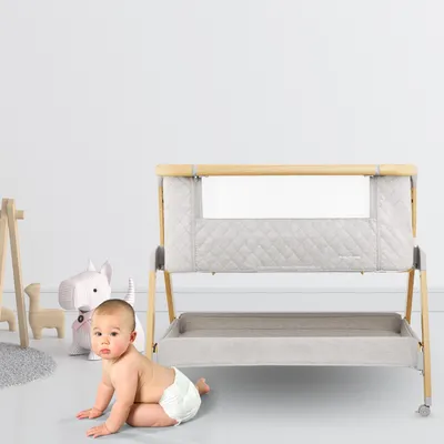 A baby is crawling on the floor next to a baby crib.
