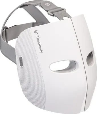 A white Therabody TheraFace Mask LED facial mask with gray straps, shown from a diagonal front view against a white background.