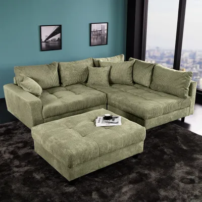 A modern green corduroy sectional sofa with an ottoman is arranged in a living room setting with artwork on the wall and a city view through a large window.