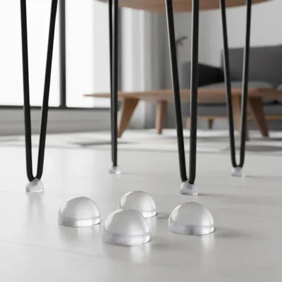 Close-up of clear silicone floor protectors under black hairpin table legs on a light-colored floor.