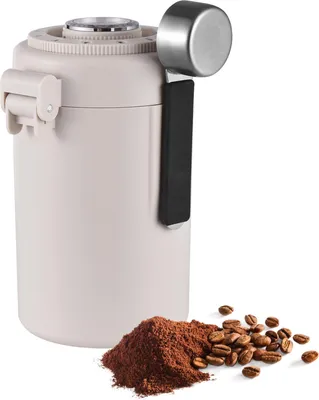 A beige coffee storage container with a scoop and a pile of coffee beans and grounds in front of it.