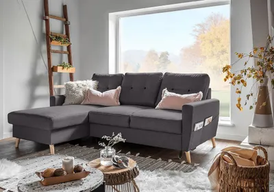 A dark gray sectional sofa with decorative pillows is placed in a living room setting with a large window overlooking autumn foliage.