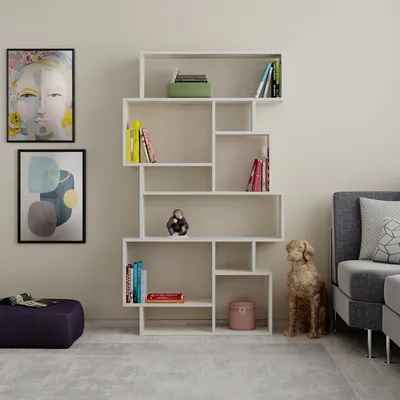 A modern living room with a white geometric bookshelf filled with books and decorative items, next to a sofa and a dog statue.