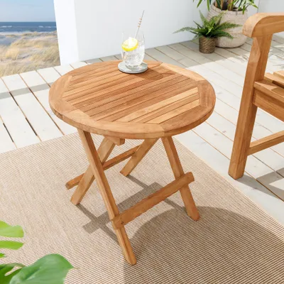 A round wooden garden table with a drink on it, placed on a patio next to a chair.