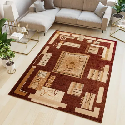 A modern rug with geometric patterns is placed on a light wooden floor in a living room setting, next to a sectional sofa and a glass coffee table with plants.