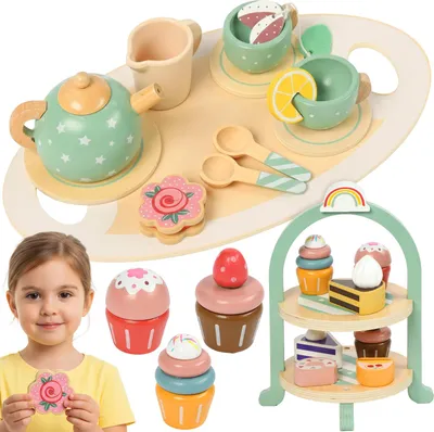 A young girl is holding a wooden flower cookie while a wooden tea set and tiered cake stand are displayed.