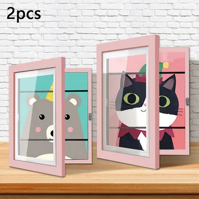 Two pink picture frames with cartoon animal drawings inside, displayed on a wooden surface against a white brick wall.