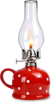 A red and white polka dot oil lamp with a glass chimney and a lit flame.