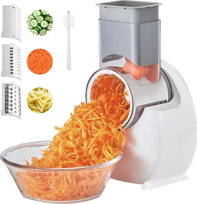 A white electric vegetable slicer with various attachments and shredded carrots in a glass bowl.