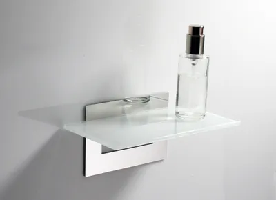 A glass shelf mounted on a white wall with a bottle of liquid on it.