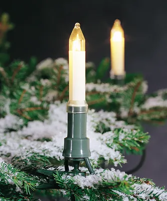 Close-up of Christmas tree lights shaped like candles, with artificial snow on the branches.