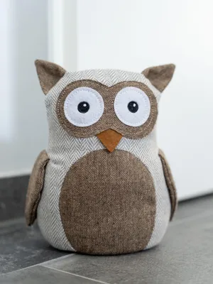 A stuffed owl doorstop sits on a tiled floor in front of a white wall.