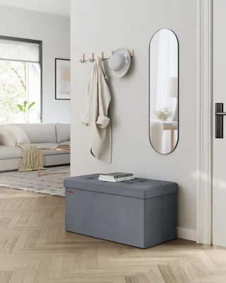 A storage ottoman in a hallway next to a coat rack and mirror.