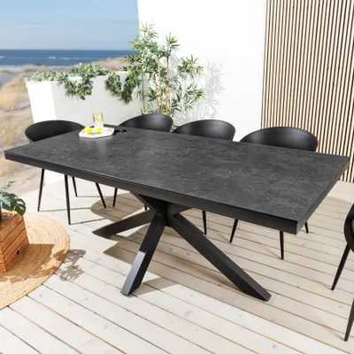 An outdoor dining table and chairs set on a wooden deck with a view of the ocean and beach.