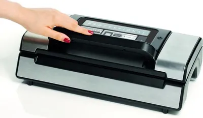 A hand is pressing a button on a vacuum sealing machine.