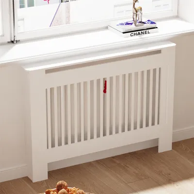 A white radiator cover with vertical slats and a shelf on top, placed in front of a window.