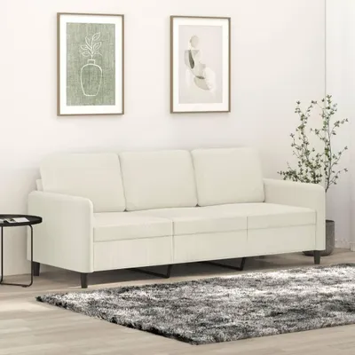 A cream-colored three-seater sofa is shown in a room with two framed pictures on the wall and a plant in a pot.
