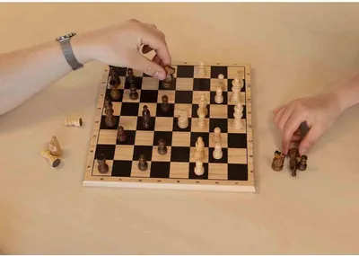Two people playing chess on a wooden board.