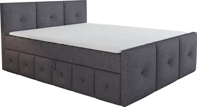 A dark gray upholstered boxspring bed with a mattress and topper, shown from a side angle.