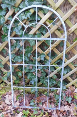 A metal garden trellis with an arched top, set against a wooden lattice fence and ivy.