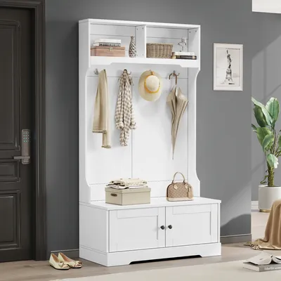 A white hall tree with a bench and storage cabinets, placed in a hallway next to a door.