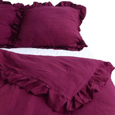 A close-up view of a burgundy duvet cover and pillowcase set with ruffled edges, laid out on a white surface.