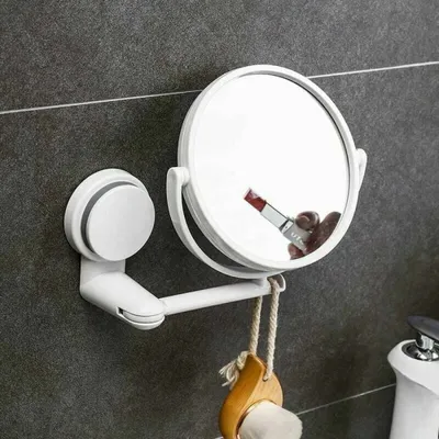 A white suction cup makeup mirror mounted on a gray tiled wall, with a makeup brush hanging from it.