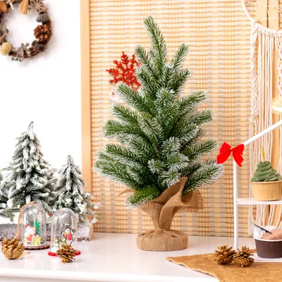A small, artificial Christmas tree decorated with white flocking and a red snowflake ornament, placed on a white surface with other Christmas-themed decorations.