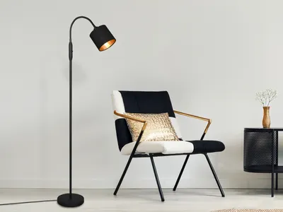 A modern black floor lamp and a black and white armchair with gold accents in a minimalist room.