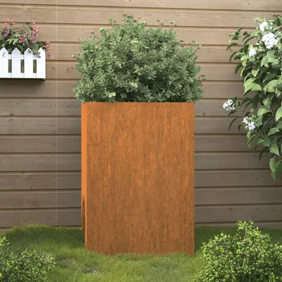 A tall, rectangular corten steel planter with a green bush inside, placed on a lawn in front of a wooden fence.
